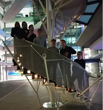 Gruppe junger Leute steht abends auf einer frei geschwungenen Treppe in einem modernen Foyer.